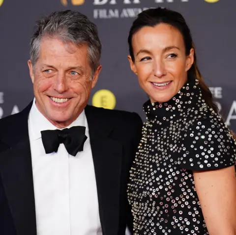 PA Media Hugh Grant and his wife Anna Eberstein; he's in a tuxedo and black bow tie and she's in a black dress with silver sequins 