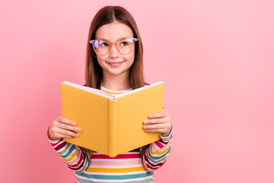 A girl wearing glasses thoughtfully holds a yellow book.