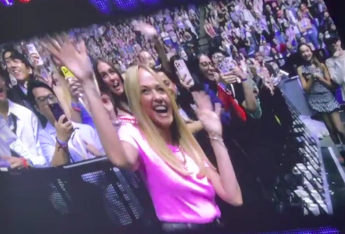 Woman in pink shirt waving at a concert.