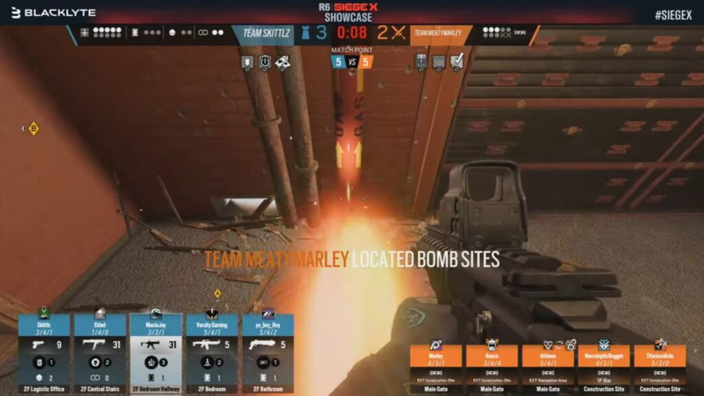 In a first-person shooter game, a player aims their weapon at an explosion, with team scores and bomb site locations displayed — a high-stakes scene from the video game Siege X