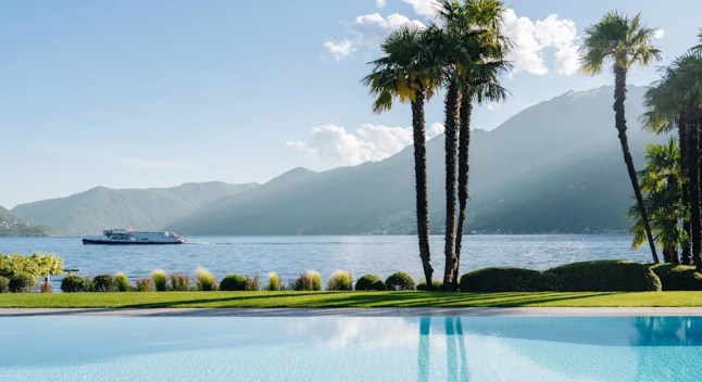 A view of Lake Maggiore from the swimming pool of the Hotel Eden Roc in Switzerland, with palm trees and mountains in the background.