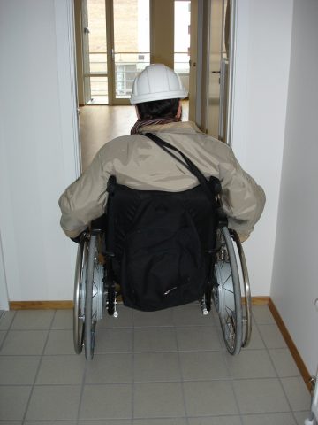 En person i rullestol forsøker å gå inn i et rom med trang dør.