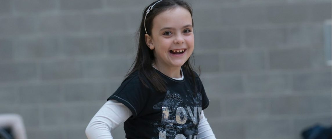 En ung jente i en gymsal smiler og ser i kamera.