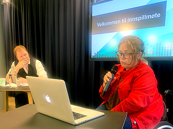 Magnhild Sørbotten snakker i mikrofon på innspillsmøte, Sigbjørn Gjelsvik ser lyttende på henne