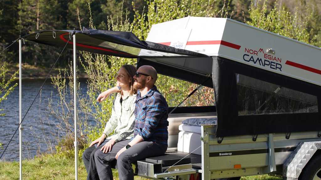 Kvinne og mann sitter på baklemmen på Norwegian Camper, under halvtak. Foto.