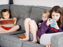 children lying on sofa and using gadgets