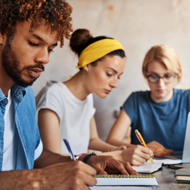 Firefly trois jeunes adultes concentrés sur leur travail à une table. Au premier plan, un homme à la