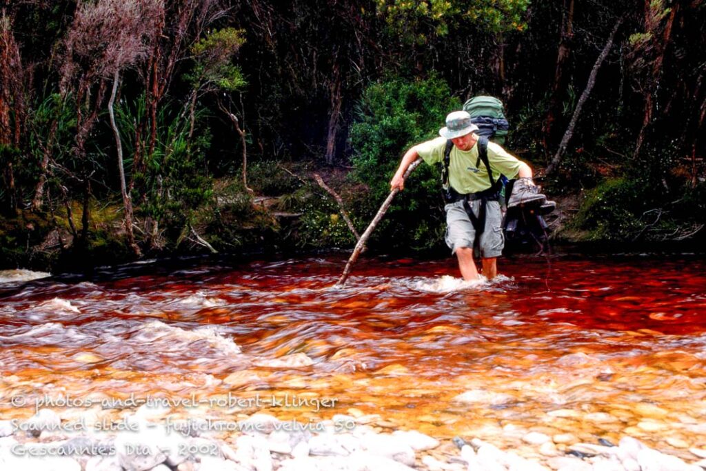 A hiker crossing a river on the port davey track, Tasmania