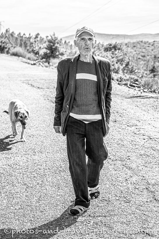 A poor man walking on a road with a dog in Albania, black and white photo