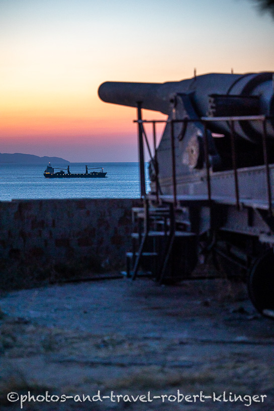 A cannon and a container ship at the street of Dardanelles in Western Turkey