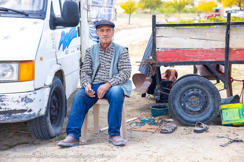 A man in Cappadocia sitting on a chair next to a car and a trailer