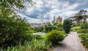 A path leads into the distance, towards a large house bordered by lush green plants at Hestercombe Gardens
