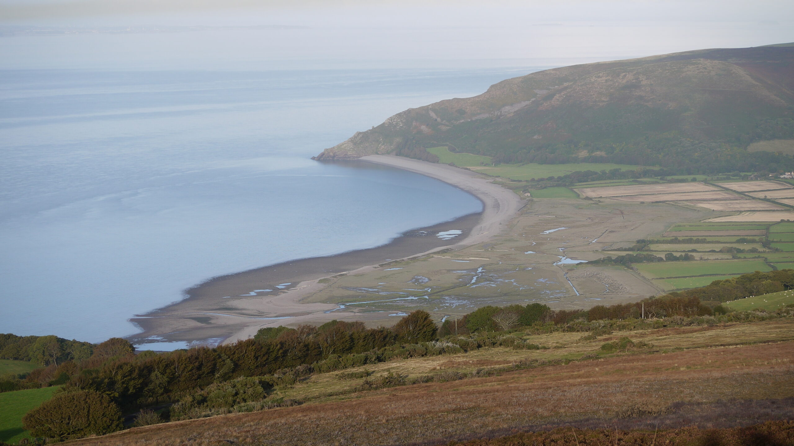 View over exmoor coast A curved bay with blue sea to the left and fields and hills to the right as views from Exmoor | Southwest Coastal Path