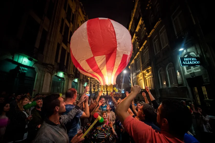 Duas pessoas, com uma multidão a assistir, lançam balão de são joão na noite do Porto
