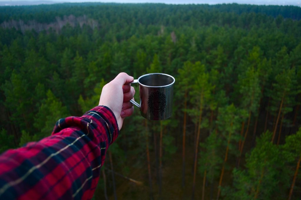 Person holding a coffie cup, with forrest background