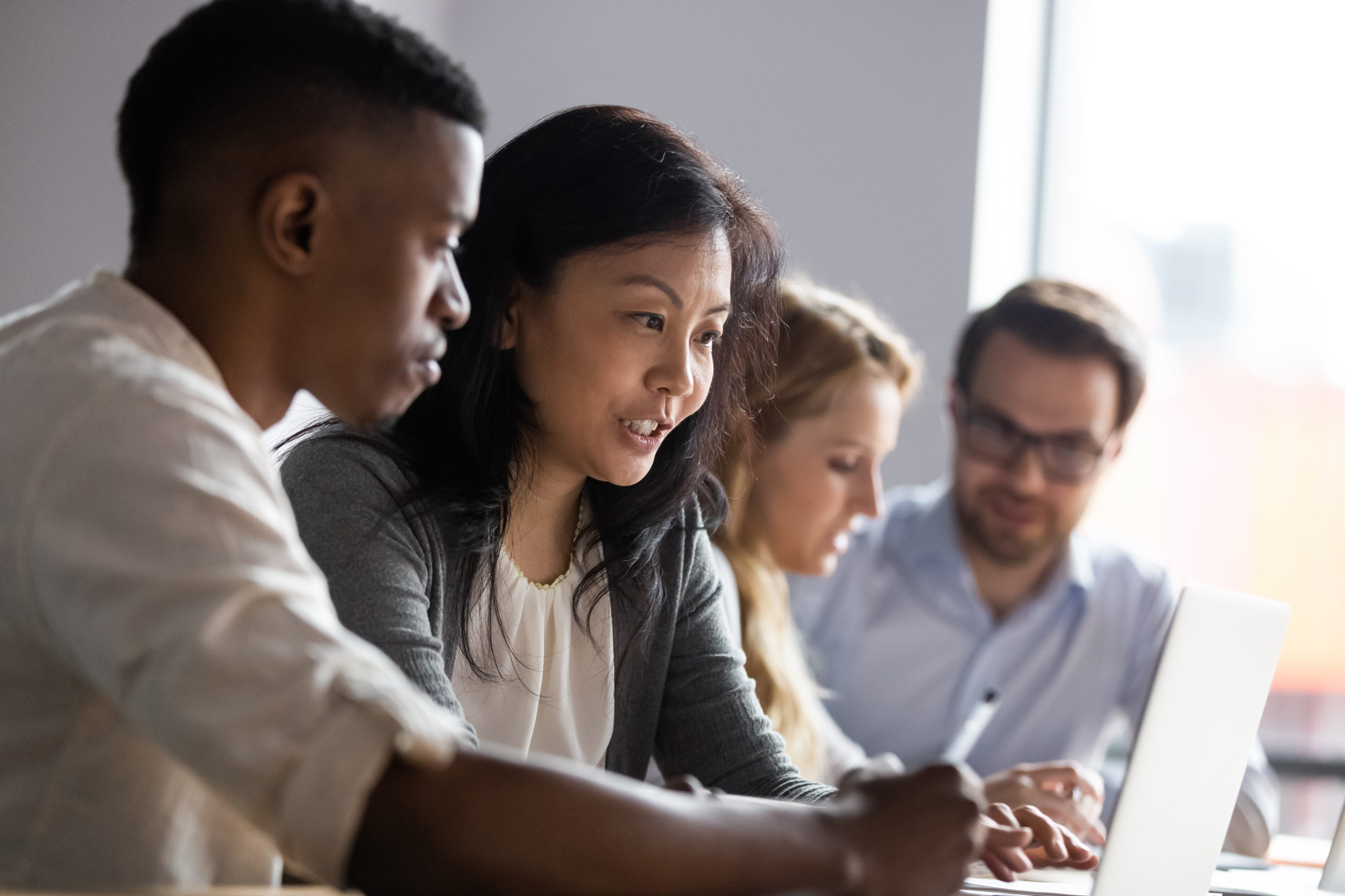 Asian businesswoman mentor teaching African American intern, helping with new corporate software, using laptop, looking at screen, diverse colleagues coworkers working on online project together