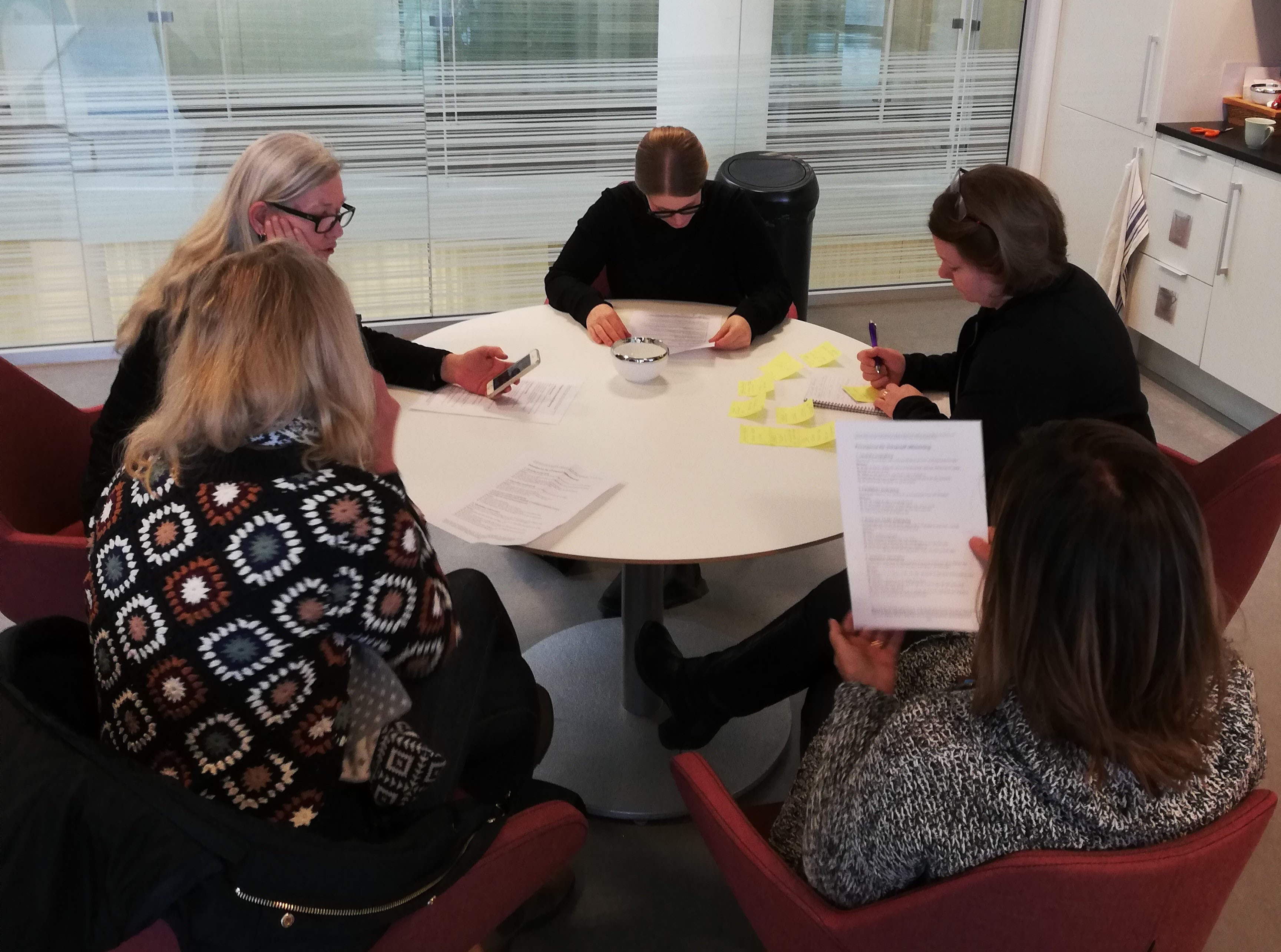 Bilden visar fem personer runt ett bord som läser och gör en gemensam uppgift