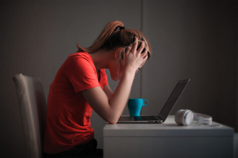 En person sitter med nedböjt huvud vid skrivbordet , med en laptop framför sig