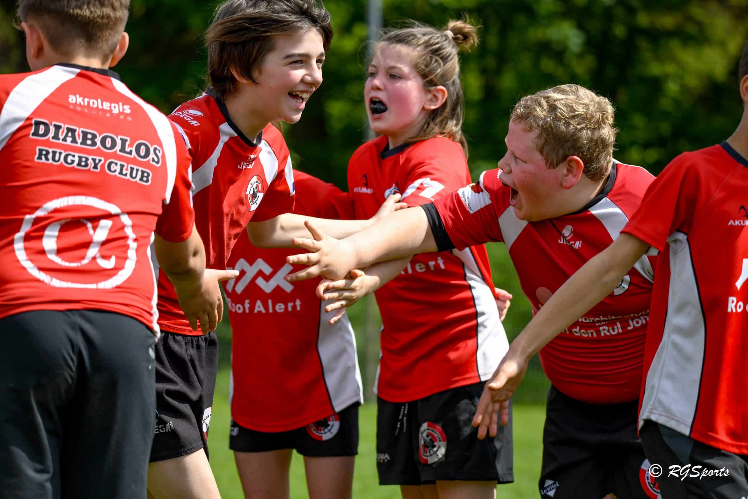 Jonge rugbyspelers van Rugby Club Diabolos Schilde vieren samen tijdens een wedstrijdmoment in volle actie.