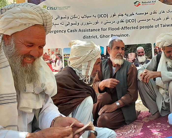 Flood-affected community members sit together during an emergency cash assistance activity implemented by Saifrood Unity and Aid Organization with support from Rebuild Aid Forening in Ghor Province, Afghanistan.