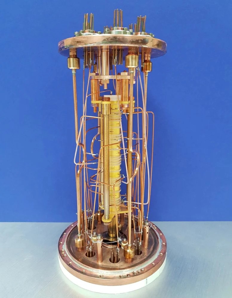 Un equilibrio atomico estremamente preciso: PENTATRAP è composto da cinque trappole Penning disposte una sopra l'altra (torre gialla al centro). In queste trappole costruite in modo identico è possibile misurare a confronto gli ioni nello stato quantico eccitato e nello stato fondamentale. Per ridurre al minimo le incertezze, gli ioni vengono anche spostati avanti e indietro tra diverse trappole per misurazioni comparative. Credito: MPIK