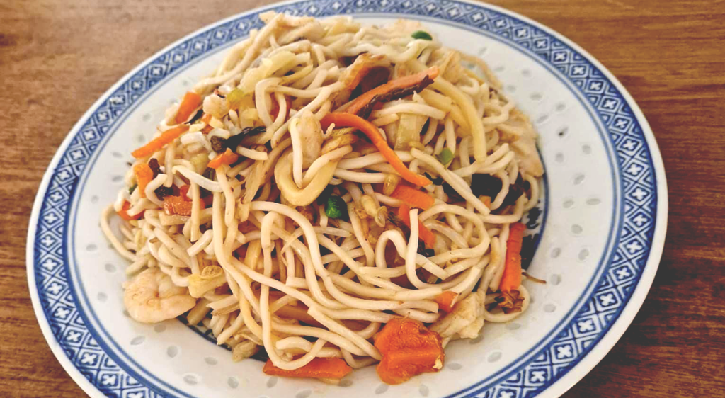 Close-up. Photo of a plate with food on a table, fried noodles with vegetables and seafood, blue pattern on the edges of the plate.