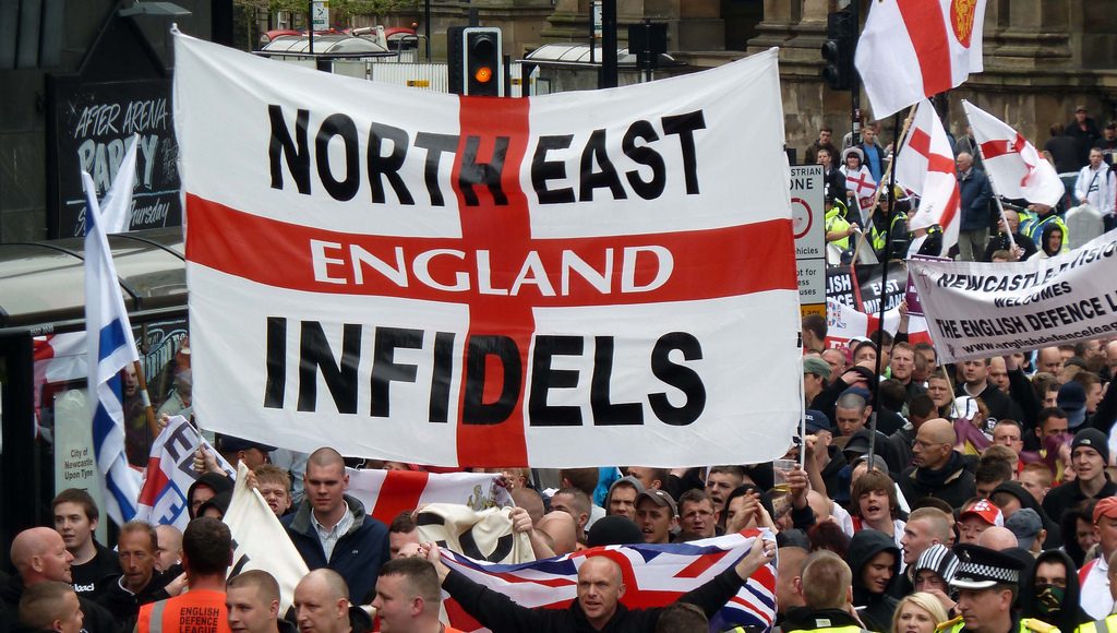 The North East Infidels at an EDL rally in 2010. People march behind a large England Flag with 'North East Infidels' written on it.