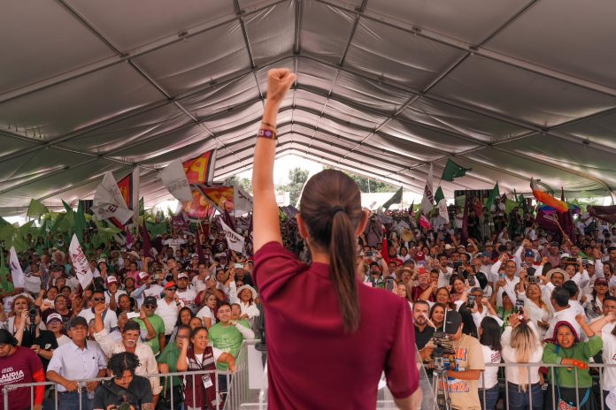 Claudia Sheinbaum raises a fist in front of an audience of MORENA supporters