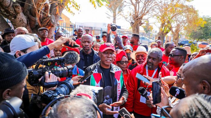 Julius Malema of the EFF speaks to a crowd of supporters and journalists with a Palestine-themed scarf draped over his shoulders