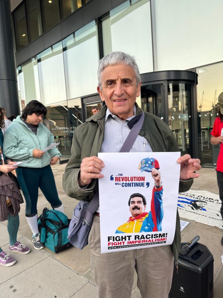 Man holds placard reading 'The revolution will continue' with a photo of Venezuela's president Nicolas Maduro waving a baseball cap. The logo of Fight Racism! Fight Imperialism! is on the placard