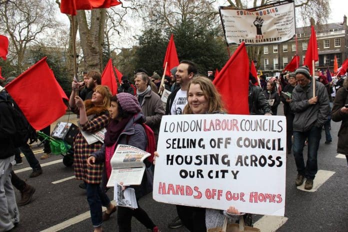 Archive photo: Activist holding a placard that reads 'London Labour Councils selling off council housing across our city - Hands off our Homes.