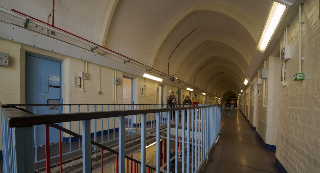 Inside HMP Reading. Long arched hall with cell doors lining it. Staircase with steel railings.