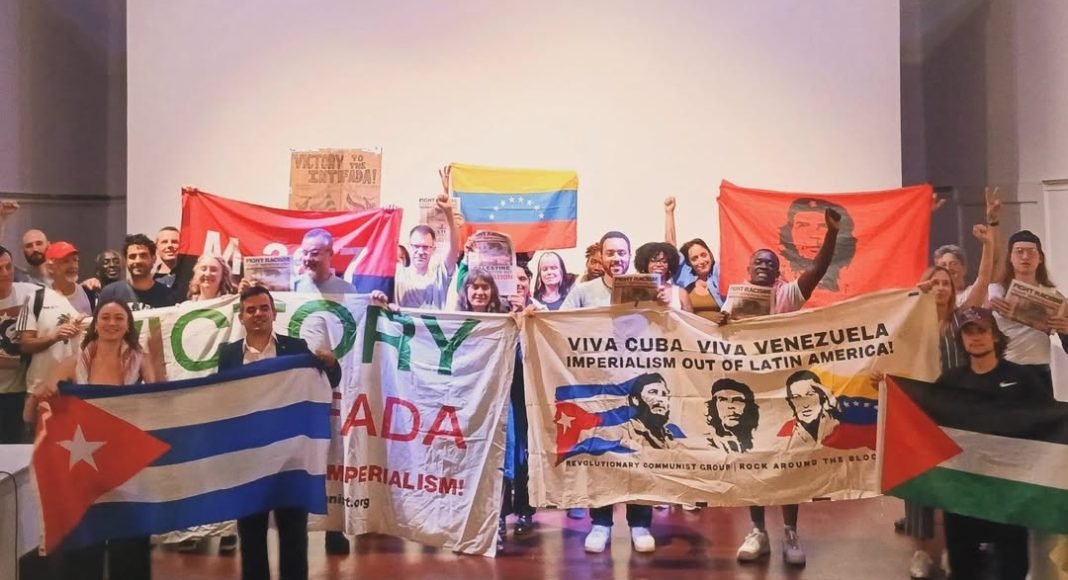 Solidarity with Cuba meeting at Bolivar Hall, 16 July 2025. Participants stand together on the stage holding up banners and flags with raised fists