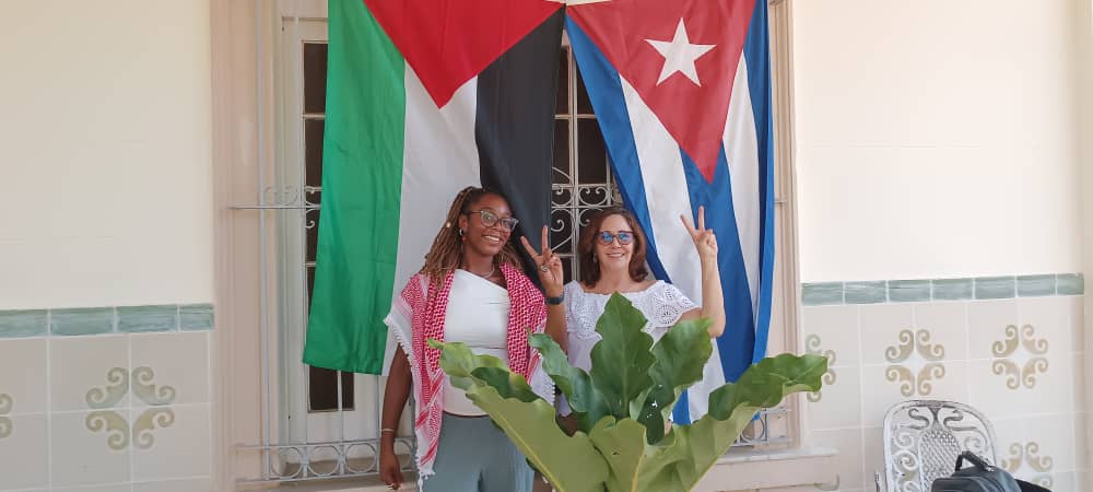 Mariela Castro and Destinie Sanchez raise their fists beneath a Palestinian and Cuban flag (photo: FRFI)
