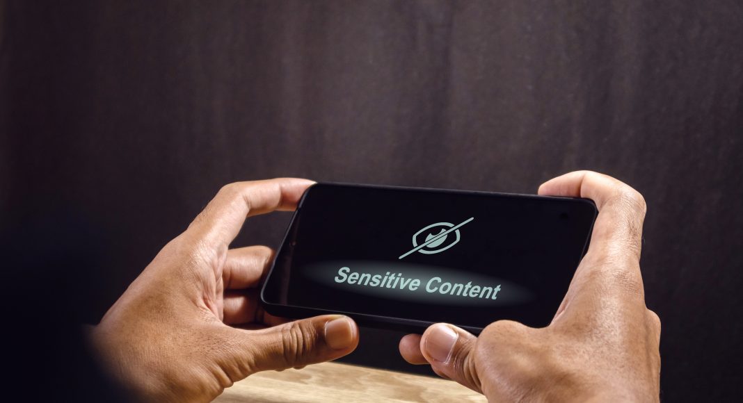Man using a smartphone with eye crossed sign on screen. Explicit content in social media or website. Restricted content.