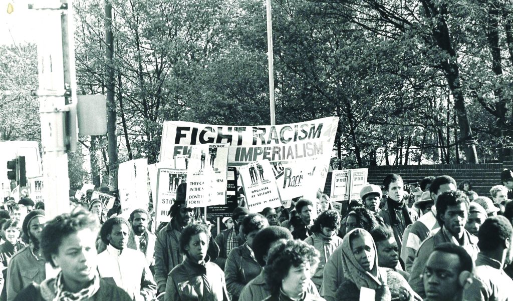 Black protesters march under banners, demand an end to state racism, black and white photograph