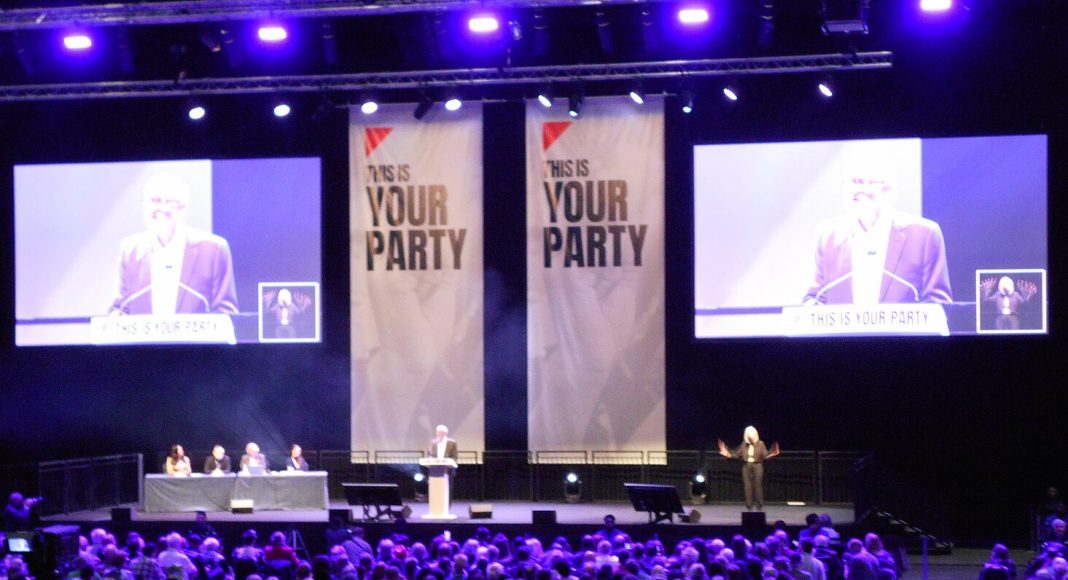Jeremy Corbyn addresses the Your Party conference hall in front of large screens and banners
