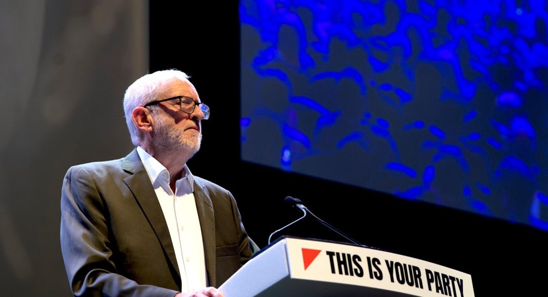 Jeremy Corbyn addresses the Your Party conference in front of screens and banners