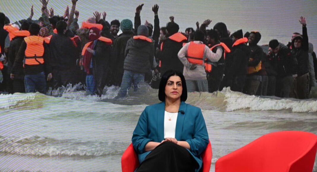 Home Secretary Shabana Mahmood sits in BBC television studio in front of an image of refugees in life jackets landing on a beach