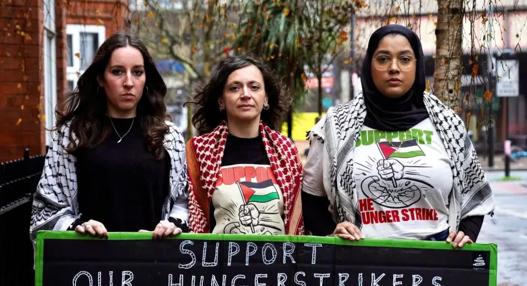 Three supporters of the hunger strikers hold a placard reading 'support our hungerstrikers' on a street