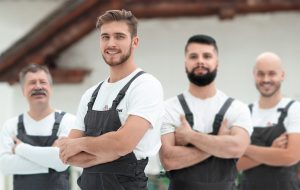 Vier Entrümpelungshelfer von Rümpelkraft in Arbeitskleidung stehen mit verschränkten Armen und lächeln – starkes Team für Haushaltsauflösungen.