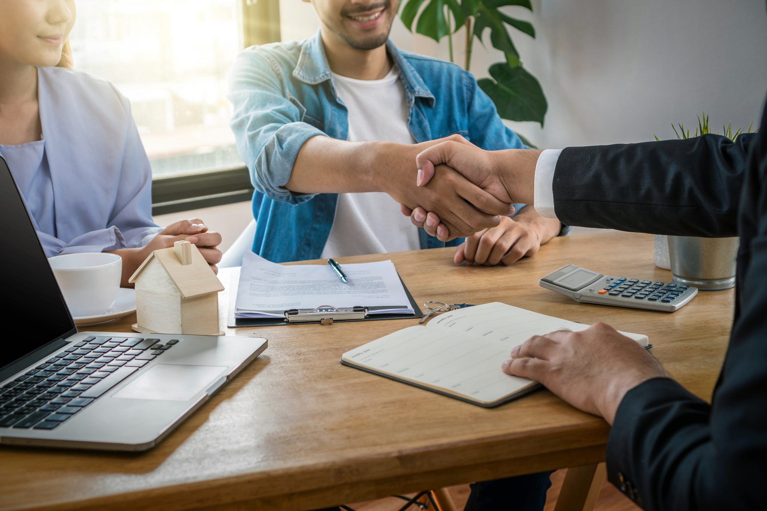 Closeup Hand shake between sale representative and house owner when sign contact of house purchase or rental on the working space table in new house,Moving and House Hunting concept,