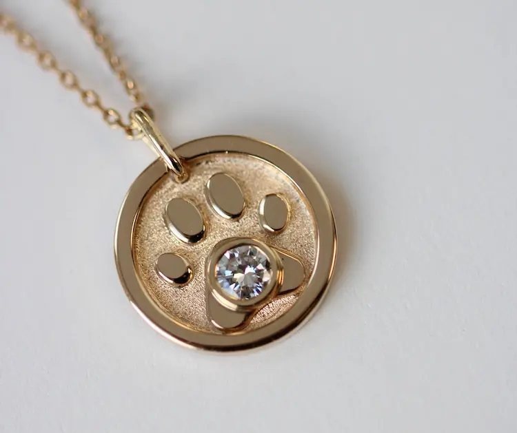 A gold pendant with a dogs paw and a colorless memorial diamond in the middle.