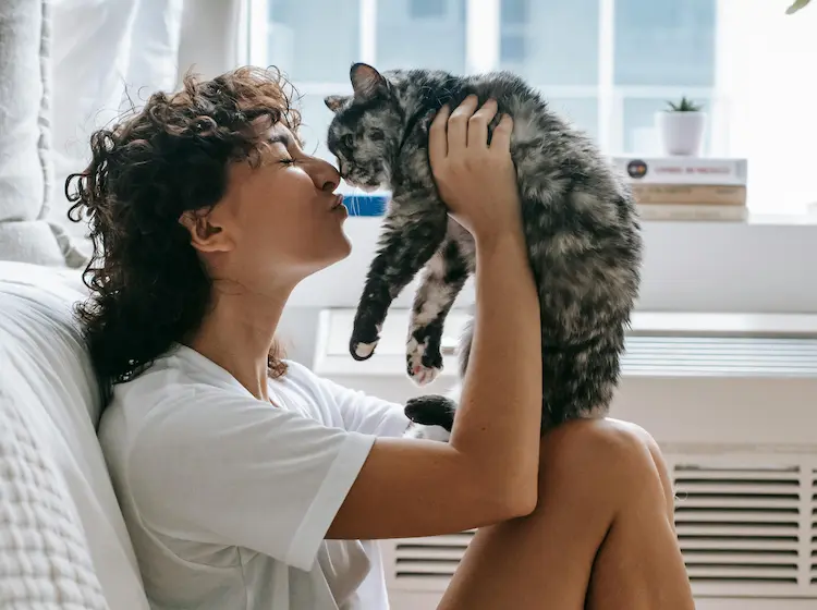 A woman, holding up a cat and kissing it.