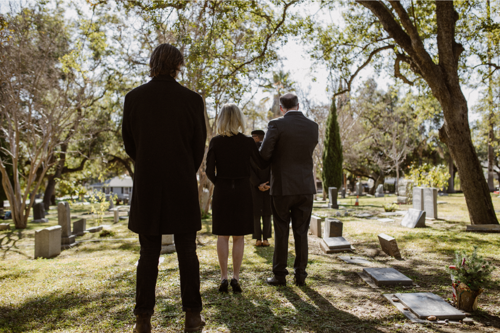 Mourners standing together in a tree-lined cemetery