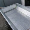 Gårdsvagnen Kellfri för ATV/traktor/klippare, med släpvagnsflak av metallisk diamantplåt och robusta däck, står parkerad på grus.