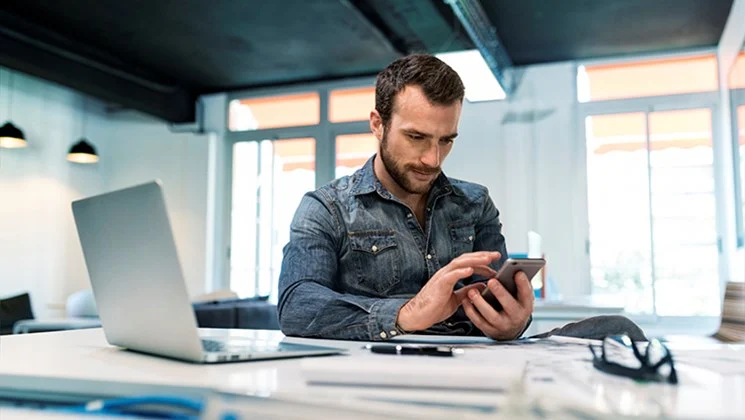 Mand der sidder på et kontor med sin computer og mobiltelefon