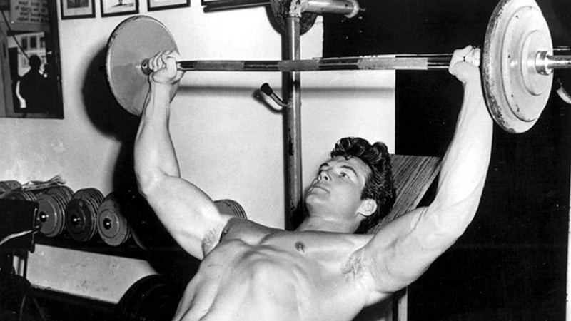 Steve Reeves réalise l'exercice de musculation du développé couché.