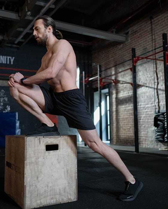 Un sportif à la salle de musculation réalise un étirement du psoas en position debout.