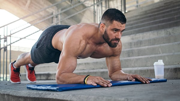 Un homme torse nu fait du gainage de face sur un tapis de fitness.